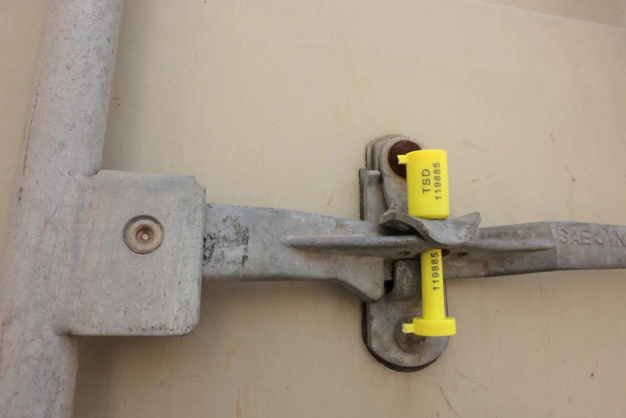 Foto do lacre amarelo número TSD 119885 preso na barra da porta do contêiner.